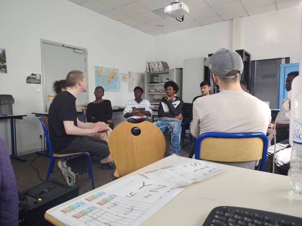 Dans une salle de classe, des élèves sont assis en cercle autour de l'artiste Gulien
